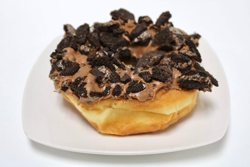 A golden-brown donut topped with chocolate frosting and crushed Oreo cookies on a white plate.