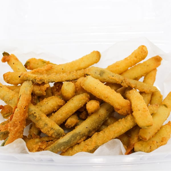 A clear plastic container filled with crispy, golden-brown fried green beans on white parchment paper.