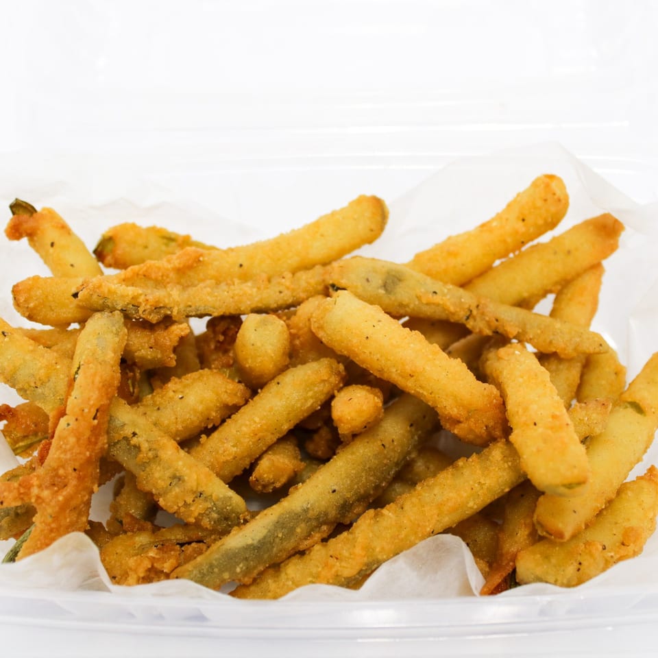 A clear plastic container filled with crispy, golden-brown fried green beans on white parchment paper.