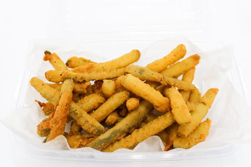 A clear plastic container filled with crispy, golden-brown fried green beans on white parchment paper.