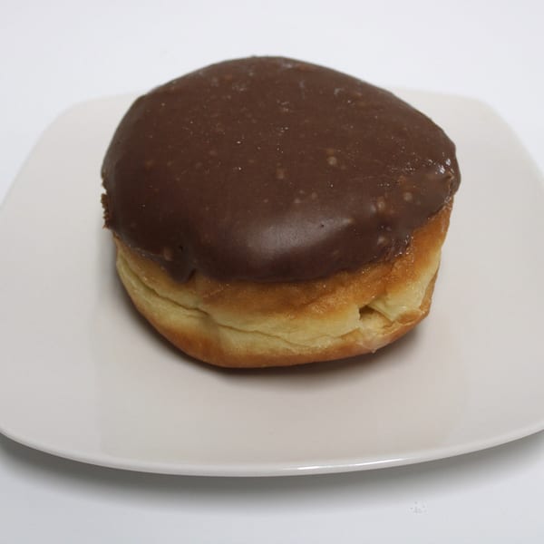 A chocolate-frosted donut with a golden-brown base sits on a white square plate.