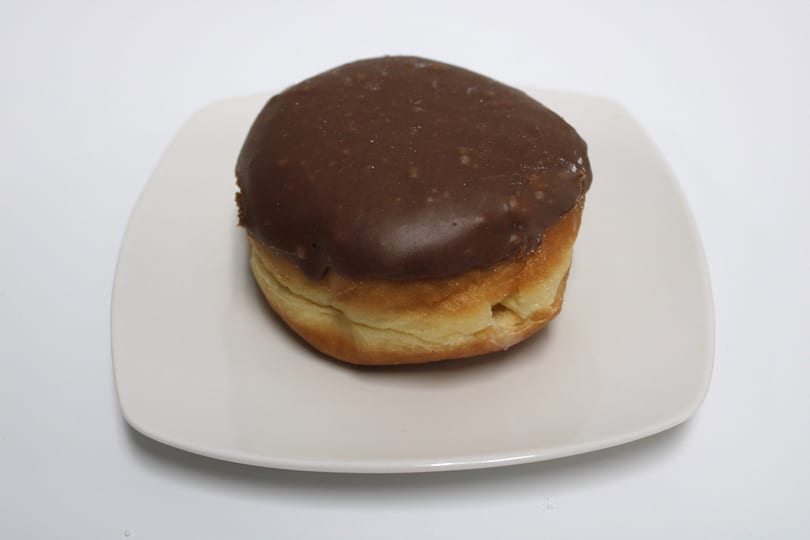 A chocolate-frosted donut with a golden-brown base sits on a white square plate.