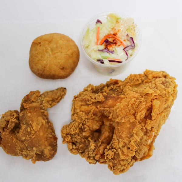 Fried chicken pieces, a biscuit, and a small container of coleslaw on a white surface.