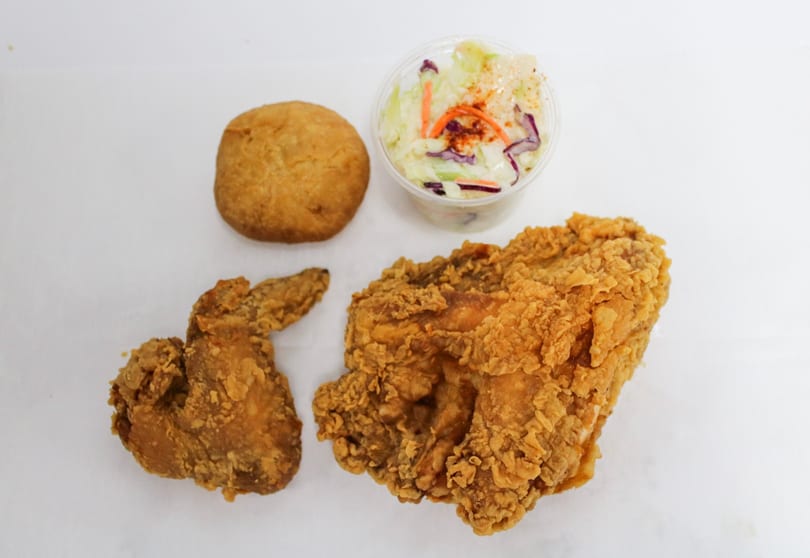 Fried chicken pieces, a biscuit, and a small container of coleslaw on a white surface.