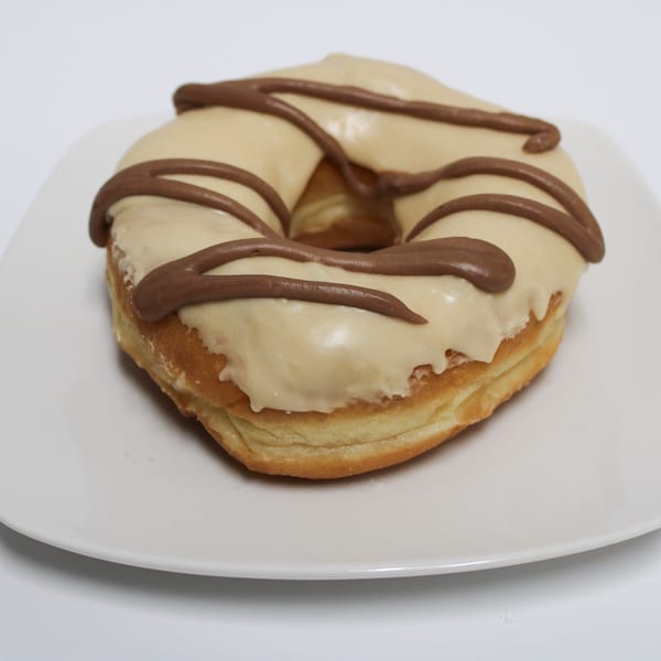 A single glazed donut with light brown frosting and dark brown drizzle on a white plate.