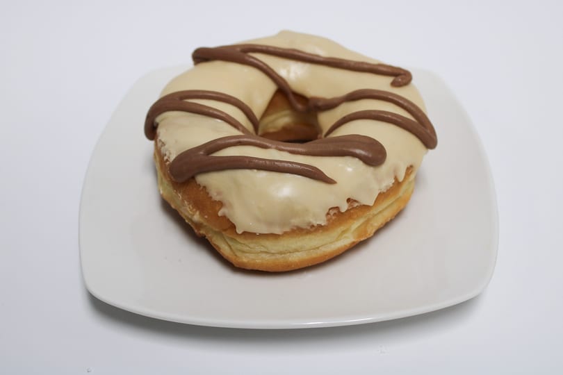 A single glazed donut with light brown frosting and dark brown drizzle on a white plate.