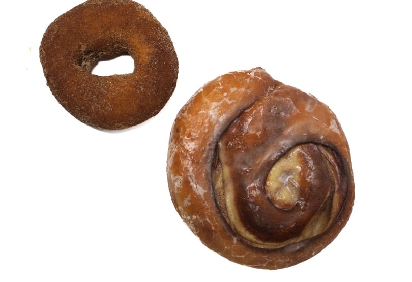 A cinnamon sugar donut and a glazed cinnamon roll on a white background.