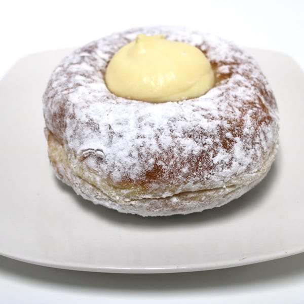 Powdered sugar donut with a dollop of yellow cream in the center, on a white plate.