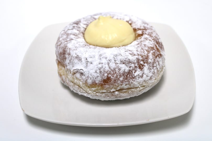 Powdered sugar donut with a dollop of yellow cream in the center, on a white plate.