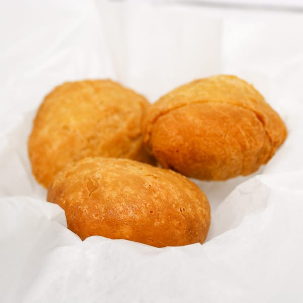 Three golden-brown fried dough balls, possibly hushpuppies or beignets, rest on white parchment paper.