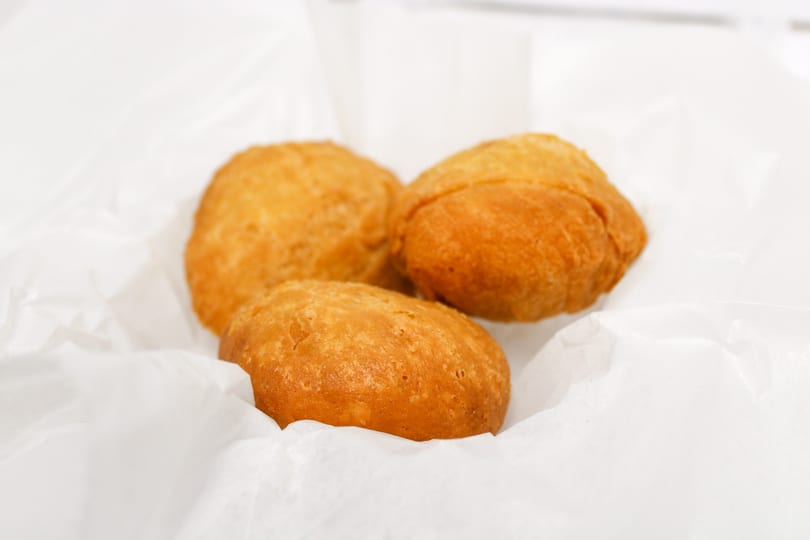 Three golden-brown fried dough balls, possibly hushpuppies or beignets, rest on white parchment paper.