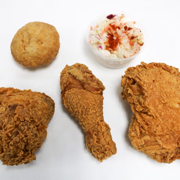 Fried chicken pieces, a biscuit, and coleslaw with paprika on a white surface.