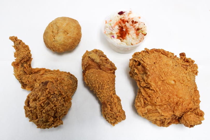 Fried chicken pieces, a biscuit, and coleslaw with paprika on a white surface.