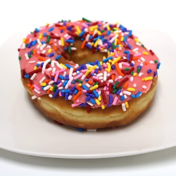 Pink frosted donut with colorful sprinkles on a white plate.
