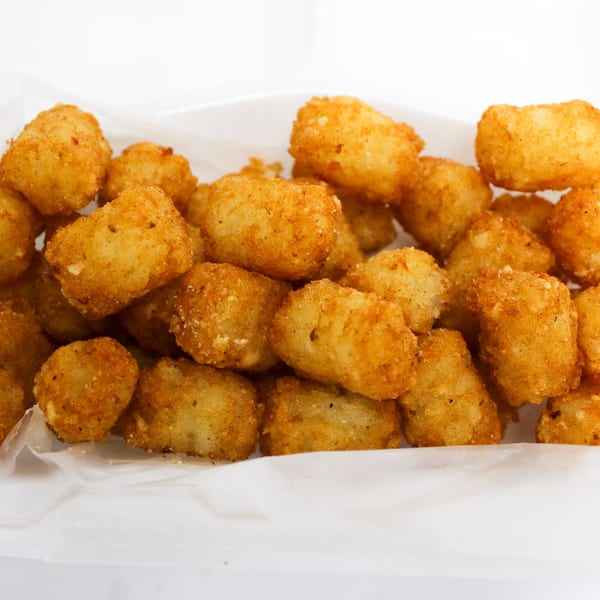 Golden brown tater tots, lightly seasoned, served in a white paper-lined container.