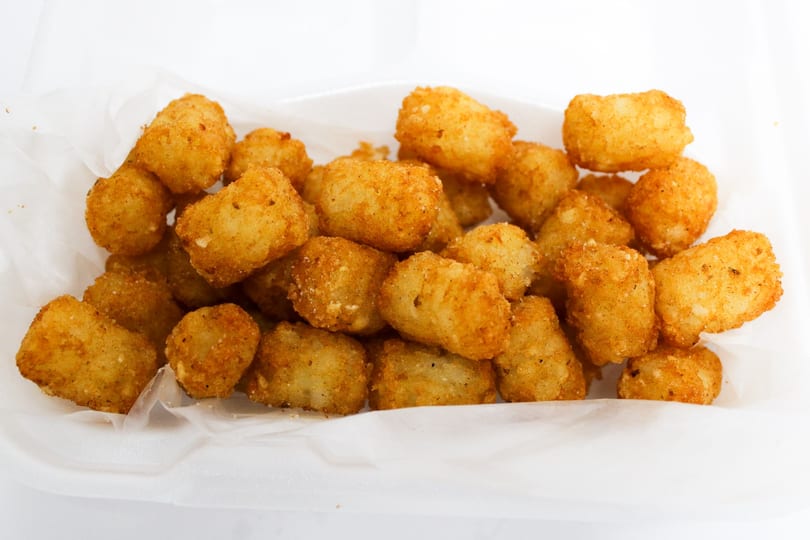 Golden brown tater tots, lightly seasoned, served in a white paper-lined container.