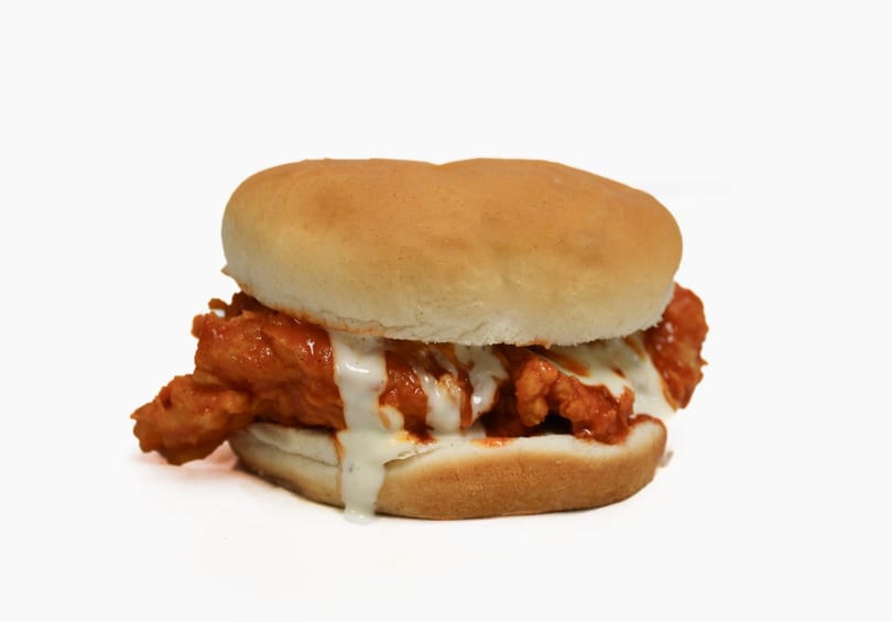 Buffalo chicken sandwich with melted cheese and ranch dressing on a white bun.