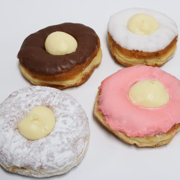 Four cream-filled donuts with chocolate, white, pink, and powdered sugar frosting on a white surface.
