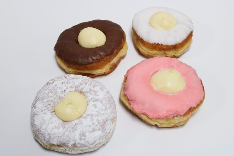 Four cream-filled donuts with chocolate, white, pink, and powdered sugar frosting on a white surface.