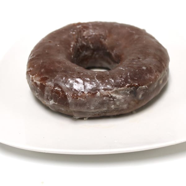 A single chocolate glazed donut sits on a white square plate against a white background.