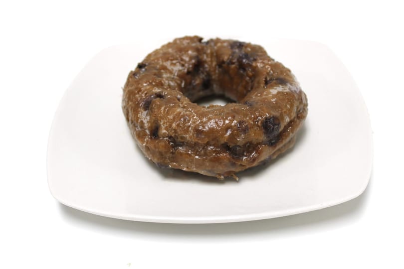 A glazed blueberry donut sits on a white square plate against a white background.