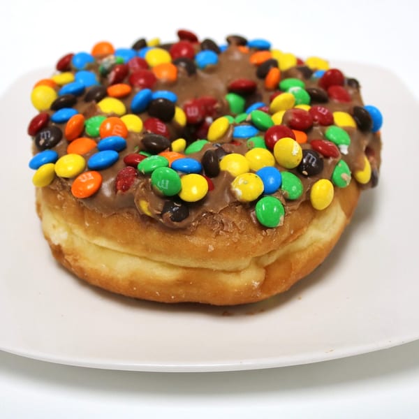 A chocolate-frosted donut topped with colorful M&M's candies on a white plate.