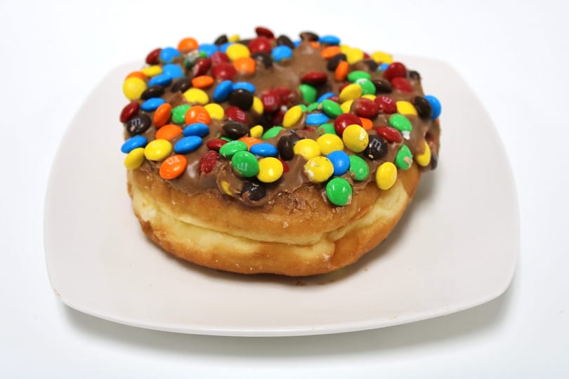 A chocolate-frosted donut topped with colorful M&M's candies on a white plate.