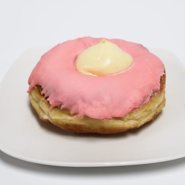 A pink-frosted donut with a dollop of yellow cream in the center, on a white plate.