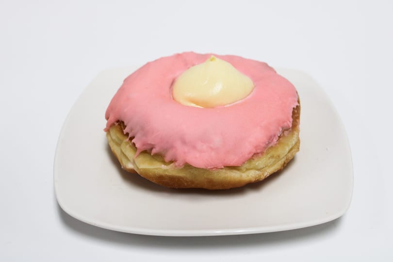 A pink-frosted donut with a dollop of yellow cream in the center, on a white plate.