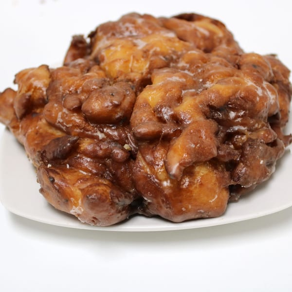 A large, glazed apple fritter with a golden-brown, craggy surface sits on a white plate.