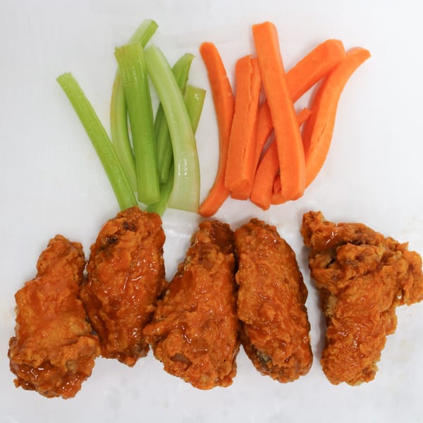 Five buffalo chicken wings with celery and carrot sticks on a white surface.