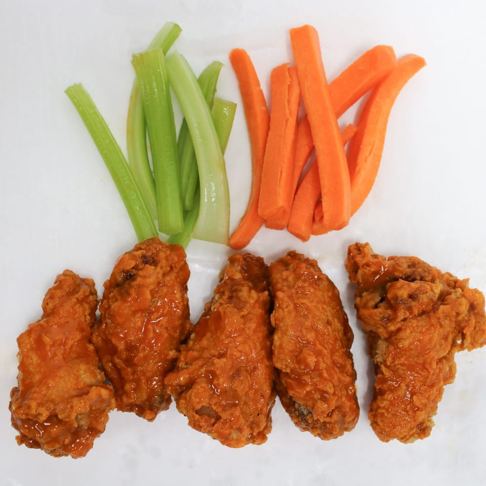 Five buffalo chicken wings with celery and carrot sticks on a white surface.