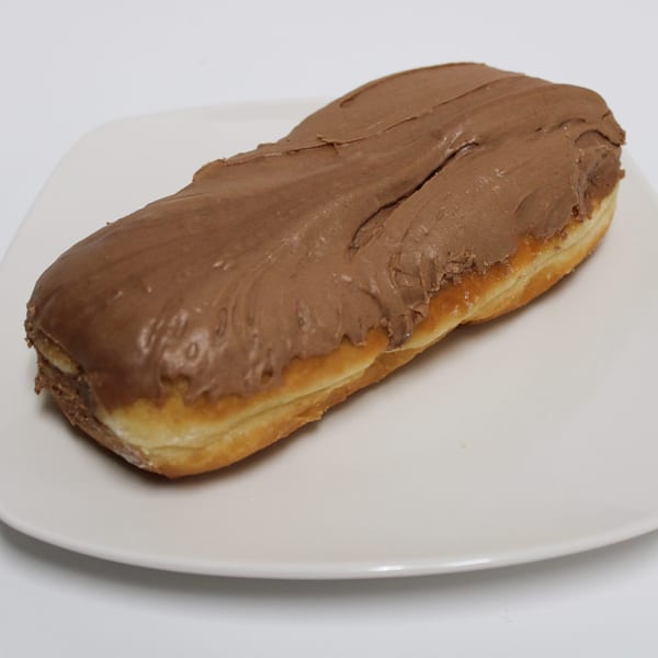 A long john donut with chocolate frosting on a white rectangular plate.