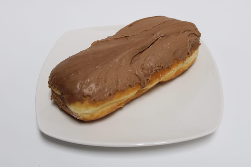 A long john donut with chocolate frosting on a white rectangular plate.