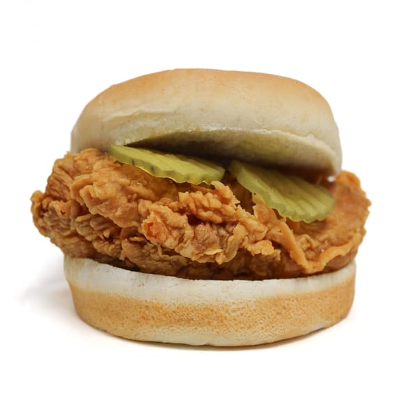 Crispy fried chicken sandwich with pickles on a white bun, isolated on a white background.