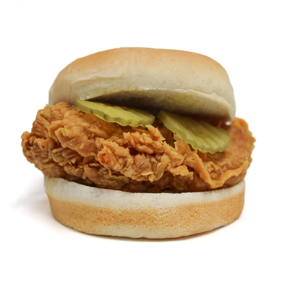 Crispy fried chicken sandwich with pickles on a white bun, isolated on a white background.
