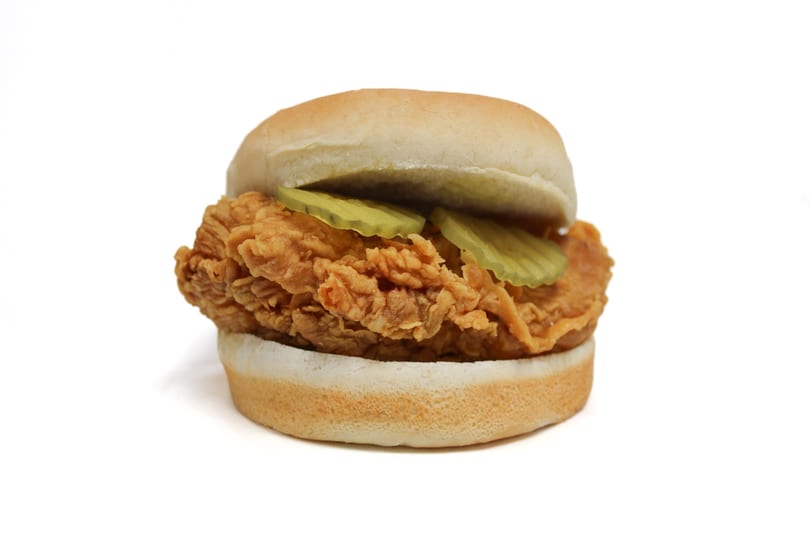 Crispy fried chicken sandwich with pickles on a white bun, isolated on a white background.