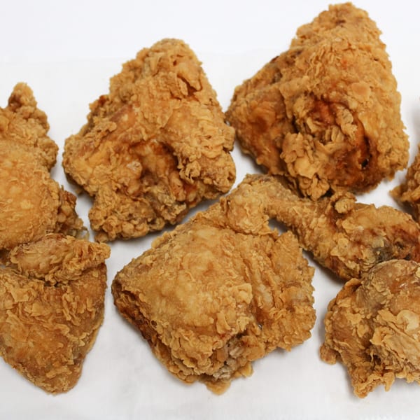 Assortment of crispy, golden-brown fried chicken pieces, including drumsticks, wings, and thighs, on a white surface.