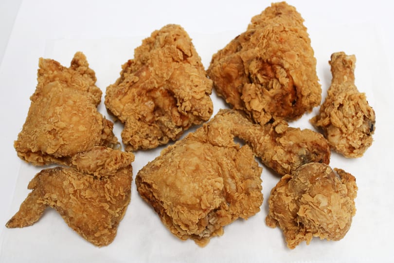 Assortment of crispy, golden-brown fried chicken pieces, including drumsticks, wings, and thighs, on a white surface.